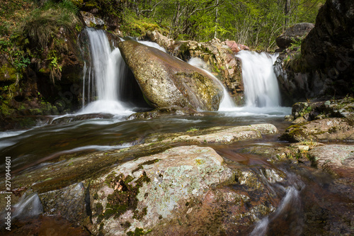 Scenic, long exposure, miniature waterfall on a mountain creek during early spring, red, vivid rocks and sunlit, green trees