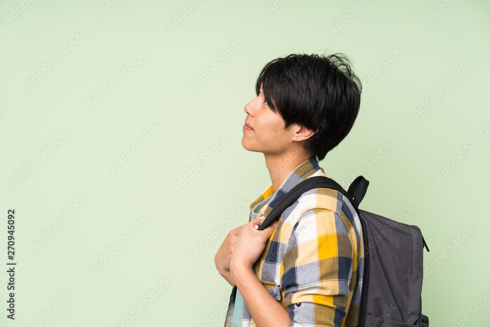 Asian man over isolated green wall with backpack Asian man over isolated green wall with backpack