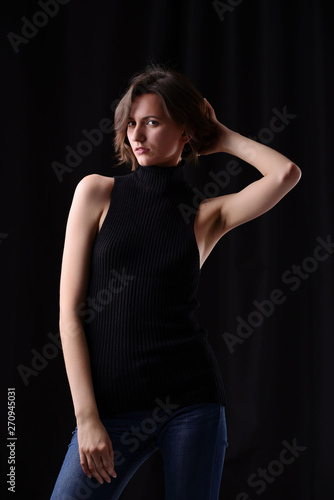 Young beautiful dark-haired girl in a black T-shirt on a dark background