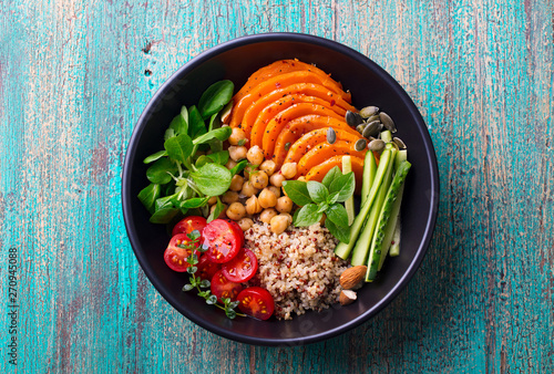 Healthy vegetarian salad. Roasted pumpkin, quinoa, tomatoes, green salad. Buddha bowl. Blue wooden background. Top view.