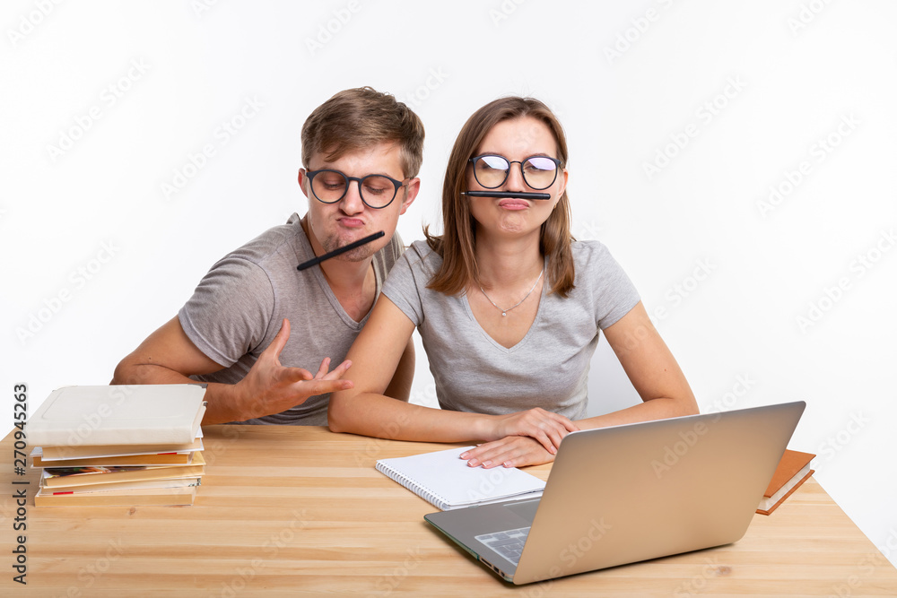 Education and people concept - a couple of young students in glasses look like they are bored of learning homework and make a stupid jokes Education and people concept - a couple of young students in glasses look like they are bored of learning homework and make a stupid jokes
