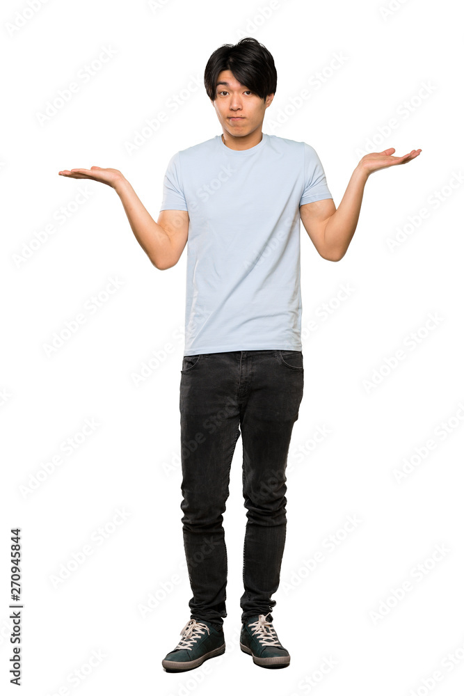 A full-length shot of a Asian man with blue shirt having doubts while raising hands over isolated white background A full-length shot of a Asian man with blue shirt having doubts while raising hands over isolated white background