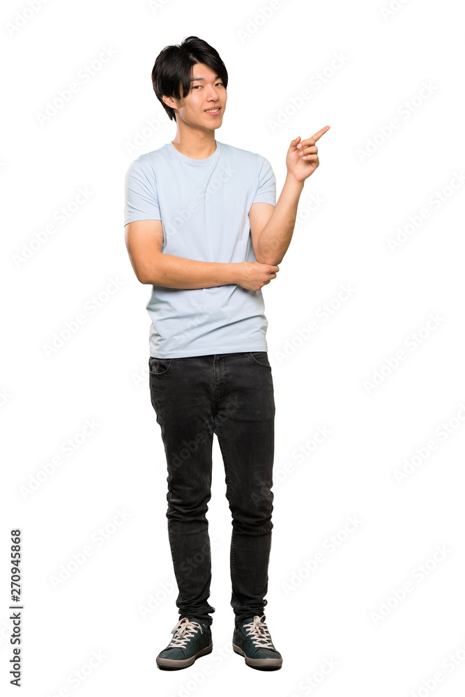 A full-length shot of a Asian man with blue shirt pointing finger to the side over isolated white background A full-length shot of a Asian man with blue shirt pointing finger to the side over isolated white background