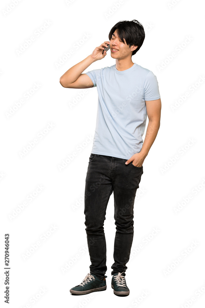 A full-length shot of a Asian man with blue shirt keeping a conversation with the mobile phone over isolated white background A full-length shot of a Asian man with blue shirt keeping a conversation with the mobile phone over isolated white background