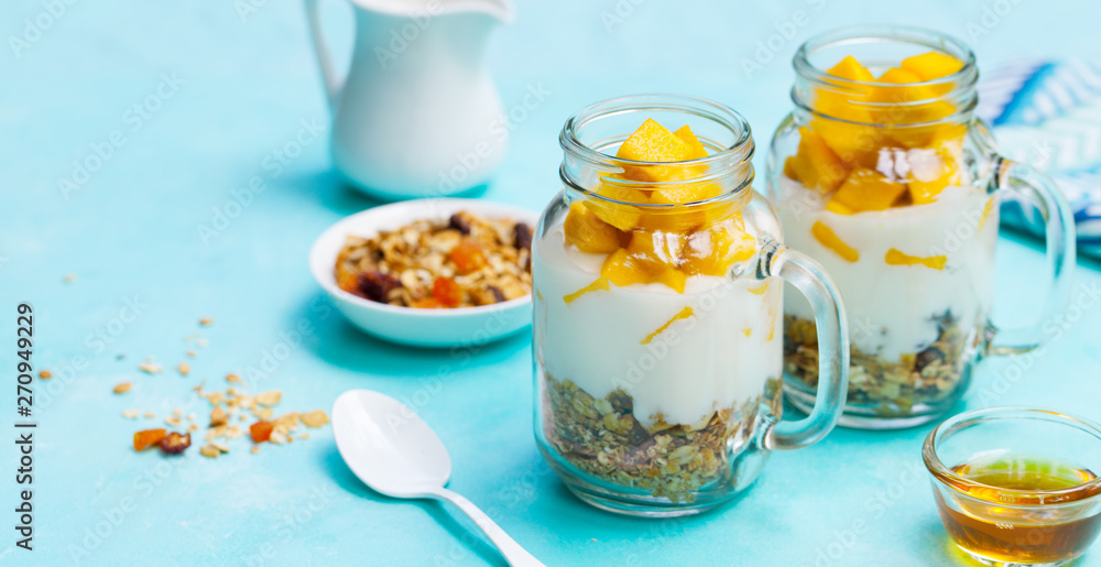 Healthy breakfast, dessert. Fresh mango fruit with yogurt and granola in jars. Blue background. Healthy breakfast, dessert. Fresh mango fruit with yogurt and granola in jars. Blue background.