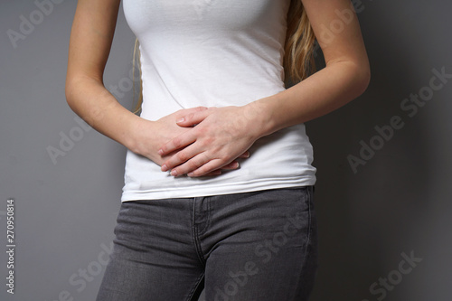 unrecognizable young woman holding her stomach with both hands - concept for dysmenorrhea, abdominal pain, irritable bowel syndrome, belly or stomach ache, painful periods or menstrual cramps
