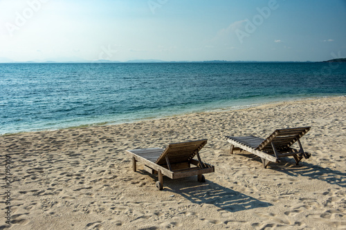 Two Wooden chairs on the white sandy beach with little waves  blue and bright blue sky.