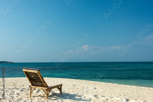 Wooden chairs on the white sandy beach with little waves, blue and bright blue sky.