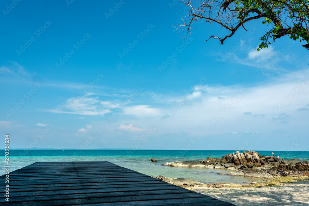 Wooden bridge for sitting on the beach resort Clear sea water with blue sky There is a small rock formation on the beach.