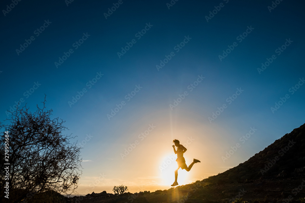 teenager running in mountains at the sunset - runner life and sportive concept - outdoor lifestyle - tree and blue background