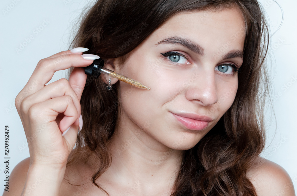 young beautiful curly woman uses gold serum for face on white background. The concept of facial skin care. young beautiful curly woman uses gold serum for face on white background. The concept of facial skin care.