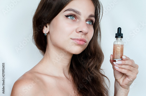young beautiful curly woman uses gold serum for face on white background. The concept of facial skin care.
