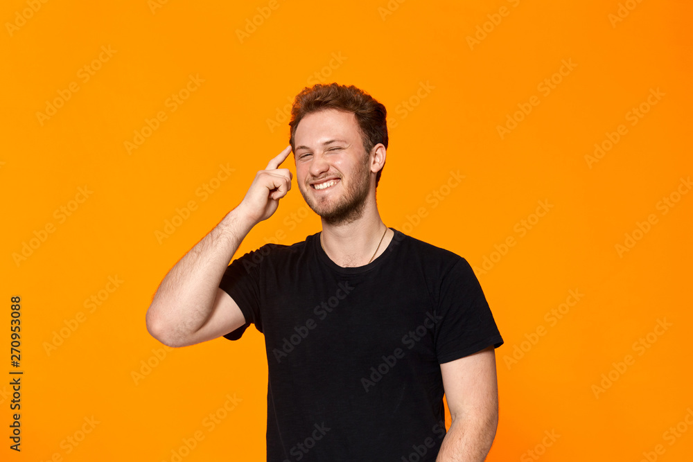 Studio shot of a bearded young man pointing a finger at the temple. Concept of a positive thinking. - obrazy, fototapety, plakaty 