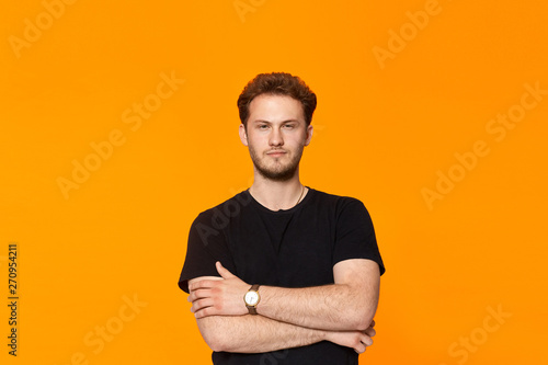 Confident handsome young man looks to the camera and keeps arms crossed