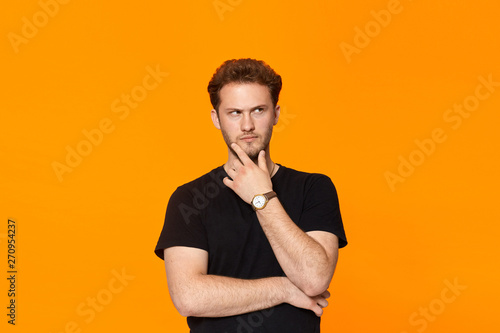 Young bearded confident man with hand raised on chin and looking at the camera.