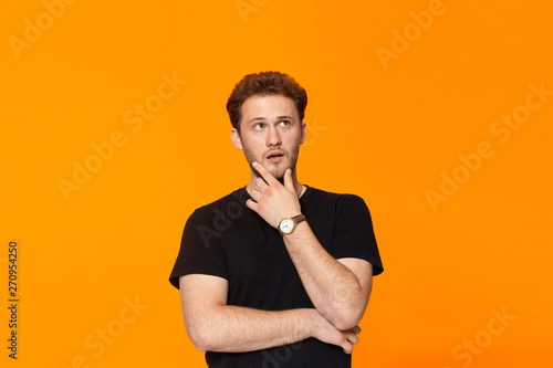 Young bearded confident man with hand raised on chin and looking at the camera.