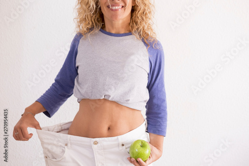 beautiful woman showing her old big pantalon after losing weight ah home - fitness at home and working to stay better with yourself - eating good with an apple in her hand photo