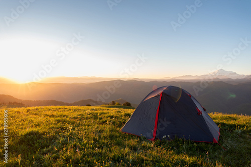 tourist tent stands on the green grass in the morning on a background of mountains