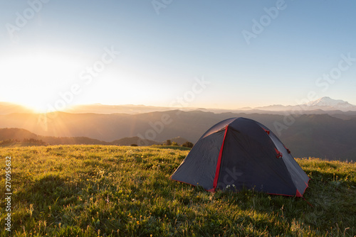 tourist tent stands on the green grass in the morning on a background of mountains © Ambartsumian