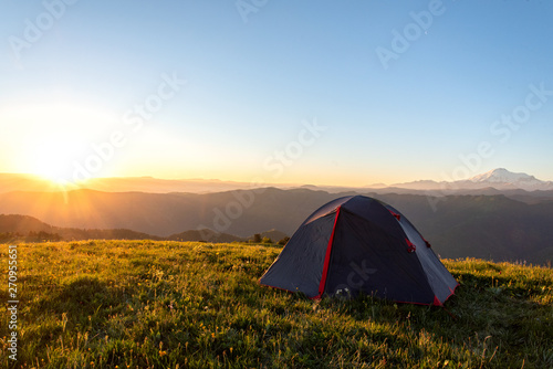 tourist tent stands on the green grass in the morning on a background of mountains