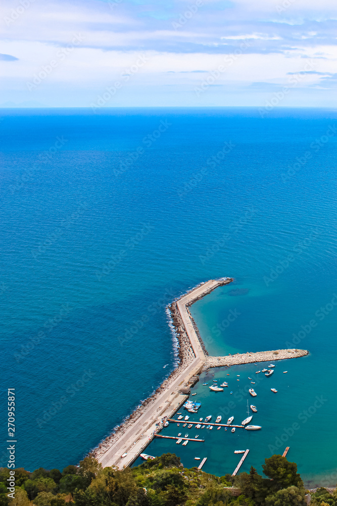 Pier in the Tyrrhenian sea by coastal Sicilian city Cefalu taken from above on a cloudy day. The wharf was taken from adjacent rocks overlooking the amazing bay. Popular Italian tourist spot