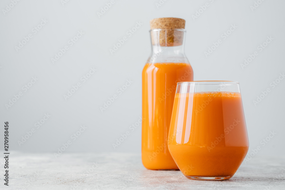 Horizontal shot of fresh carrot juice in glass containers, rich with vitamins, isolated on white wall with empty space. Vegetable drink