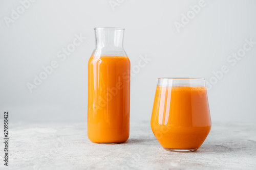 Fresh squeezed carrot juice in bottle and glass on wooden table isolated over white background. Vegetable beverage. Healthy drink.