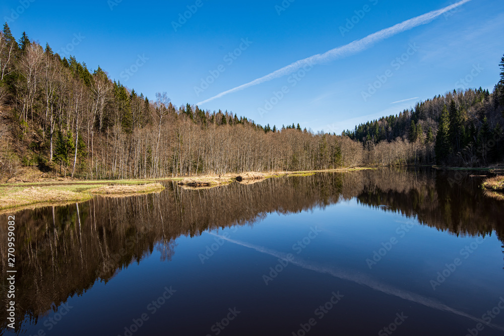calm countryside lake river with cloud reflections in water and green shores