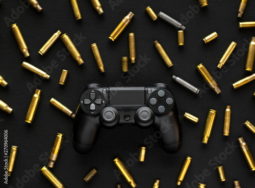 Modern black gamepad on a black background among the spent cartridges. Game concept. Shooter game.