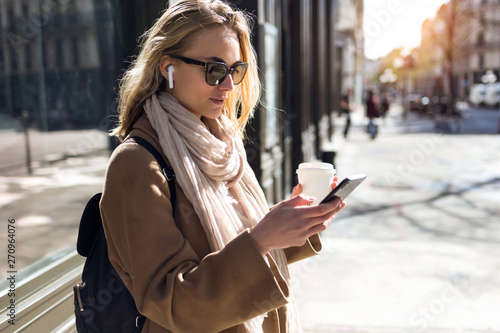 Pretty young woman listening to music with wireless earphones and the smartphone in the street. photo