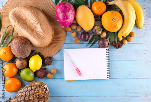 Tropical Fruits and hat with notebook with copy space over wooden background in tropical traveln theme photo