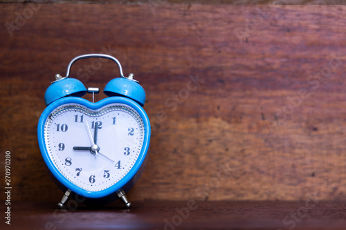 Heart shaped alarm clock on wooden background. Nine O Clock