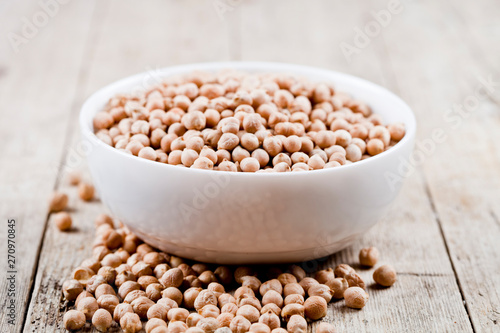 Fresh raw organic chickpeas in white ceramic bowl on rustic wooden table background.