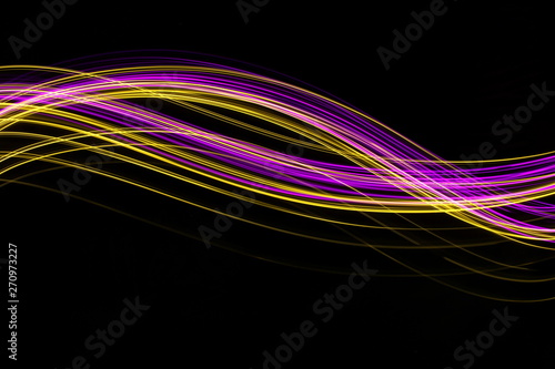 Long exposure, light painting photography. Vibrant neon pink and gold streaks of colour against a black background