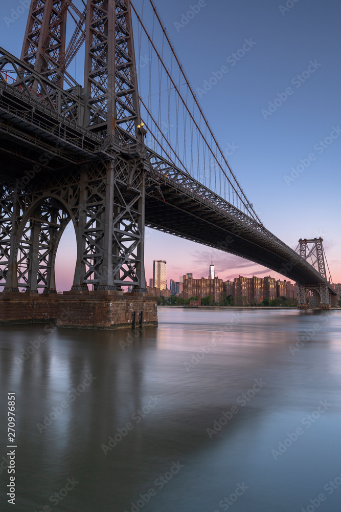 Fototapeta premium Williamsburg Bridge and Financial district view from East River at sunrise with long exposure