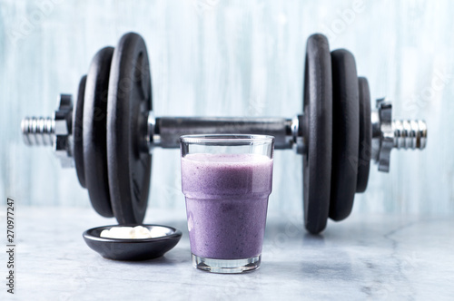 Glass of Protein Shake with milk and blueberries, Beta-alanine capsules and a dumbbell in background. Sports bodybuilding nutrition. Stone / Wooden background. Copy space. 