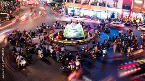 Time-lapse Aerial view, there are people and vehicles light trails crowd on busy intersection locating next to Hoan Kiem lake in old quarter of Hanoi capital at night..