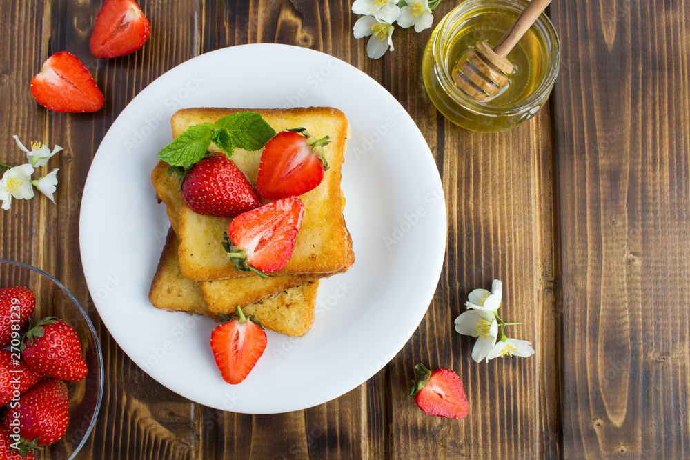 French toasts with  strawberries and honey in the white  plate on the rustic wooden background.Top view.Copy space.Closeup.