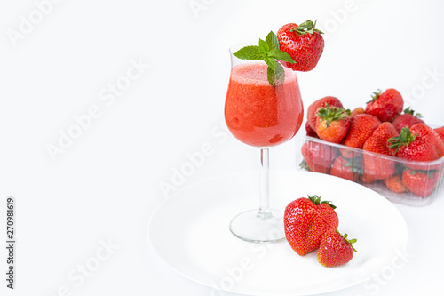 Strawberry smoothie in a glass on a high leg decorated with strawberries and mint on a white background. Strawberry season.Healthy lifestyle.