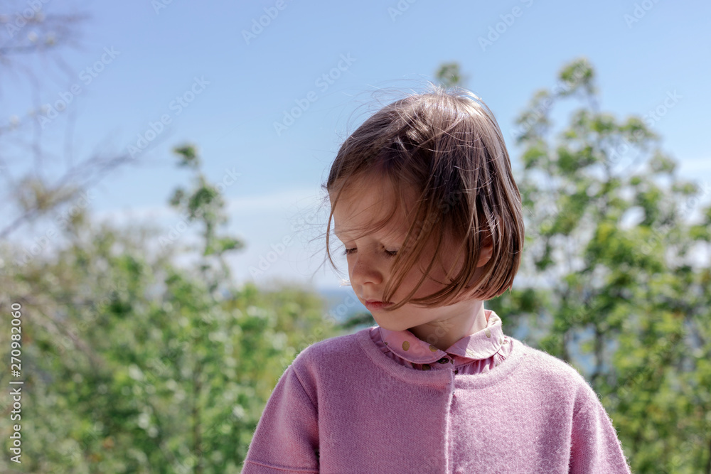 Little cute girl (7 years old) is standing against the sea in a pink outfit.