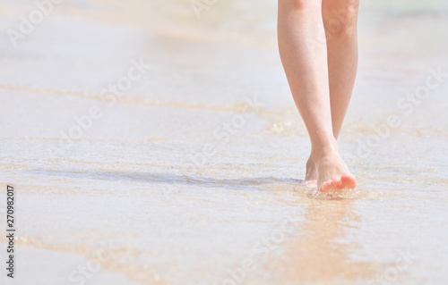 Feet girl barefoot walking by the sea. The girl touches the foot of the water.