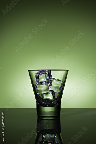 glass with ice cubes on green background