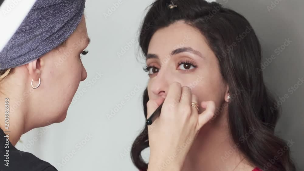 Closeup timelapse shot of cute young female makeup artist enjoying working with a beautiful young mixed race brunette model with vintage hairstyle, applying fresh trendy makeup on her face using Closeup timelapse shot of cute young female makeup artist enjoying working with a beautiful young mixed race brunette model with vintage hairstyle, applying fresh trendy makeup on her face using