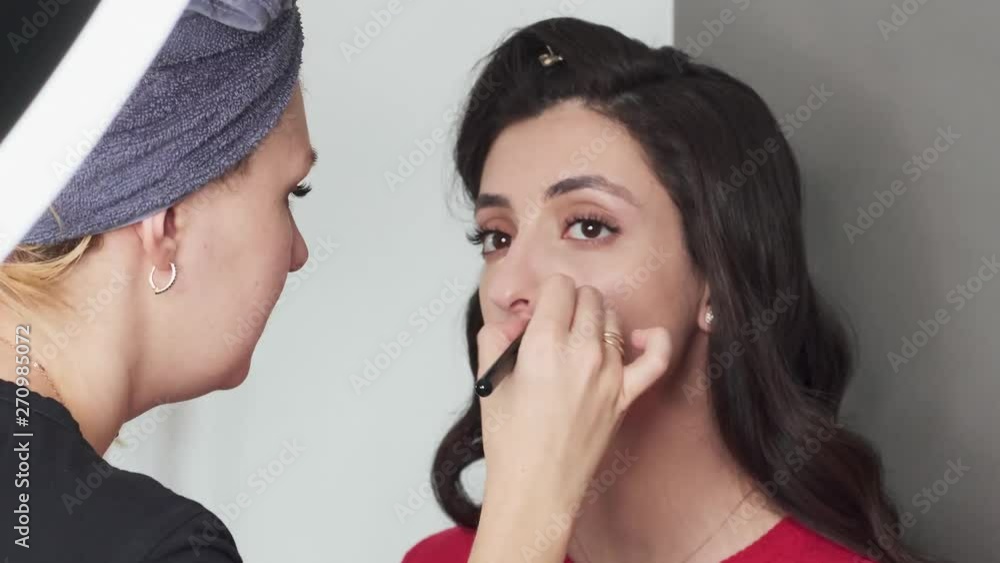 Closeup timelapse shot of cute young female makeup artist enjoying working with a beautiful young mixed race brunette model with vintage hairstyle, applying fresh trendy makeup on her face using Closeup timelapse shot of cute young female makeup artist enjoying working with a beautiful young mixed race brunette model with vintage hairstyle, applying fresh trendy makeup on her face using