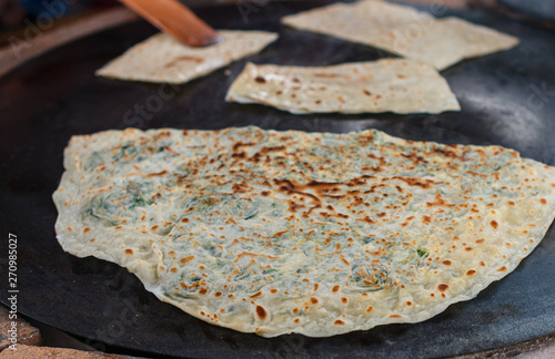 Turkish woman prepares Gozleme - traditional dish in the form of flatbread stuffed with greens and cheese, wrapped inside. Baked in a pan called a saj. Selective focus photo