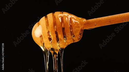 Close up honey flowing from wooden dipper on black