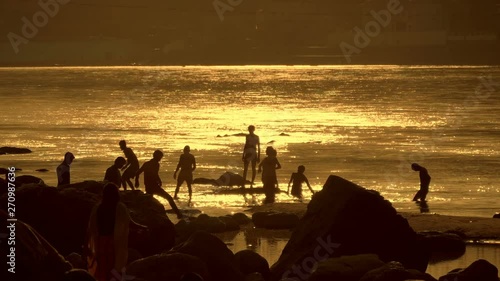 Teenagers have fun, bathe and splash into each other in the sacred Ganges River in the reflected yellow light of sunset from the water. Slow mo, slo mo, slow motion, high speed camera photo