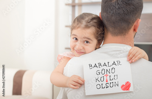 Turkish text, happy fathers day. girl showing message at fathers shoulder