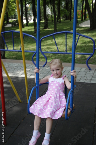 girl in a pink dress in white large polka-dot riding on a swing