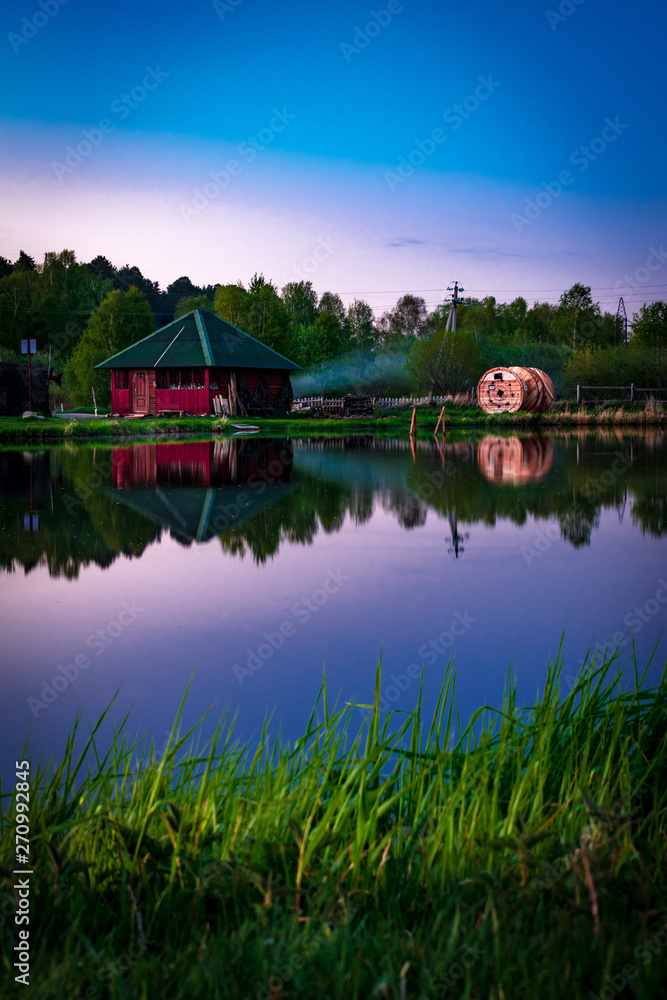 Fototapeta premium Small village red houses reflects in clearly still water at evening after sunset